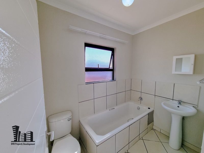 A clean, functional bathroom featuring a pedestal basin, built-in bathtub, and toilet with neutral wall and floor tiling.