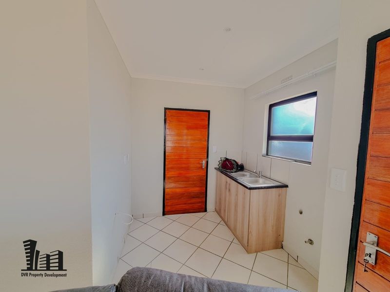 A clean and functional scullery area featuring tiled flooring, built-in cabinetry with a sink, and a timber door.