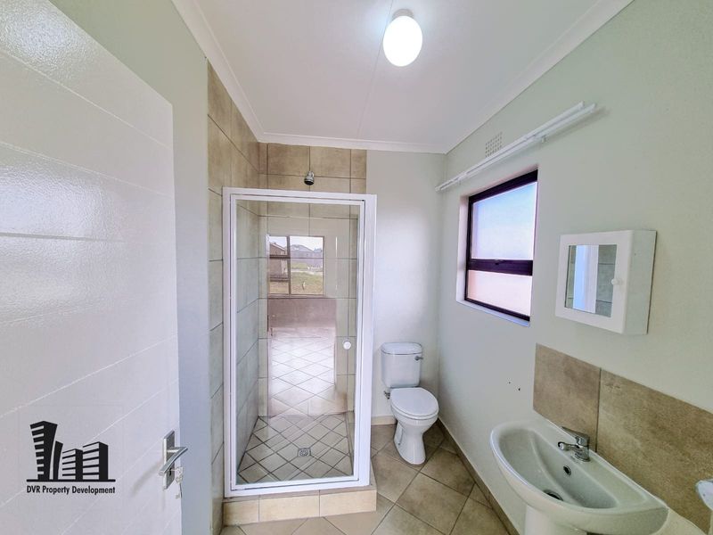 A clean and functional bathroom featuring a shower enclosure, pedestal basin, and toilet with neutral tiled flooring and wall accents.