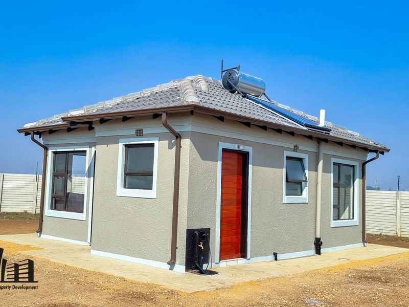 A modern, well-maintained single-story house featuring a tiled roof, solar water heating system, and aluminium window frames, set within a secure perimeter.