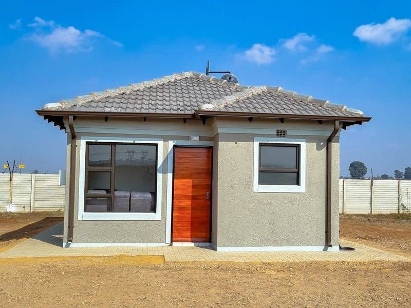 A modern single-story house exterior featuring a tiled roof, aluminium window frames, and a timber entrance door, set on a paved plot.
