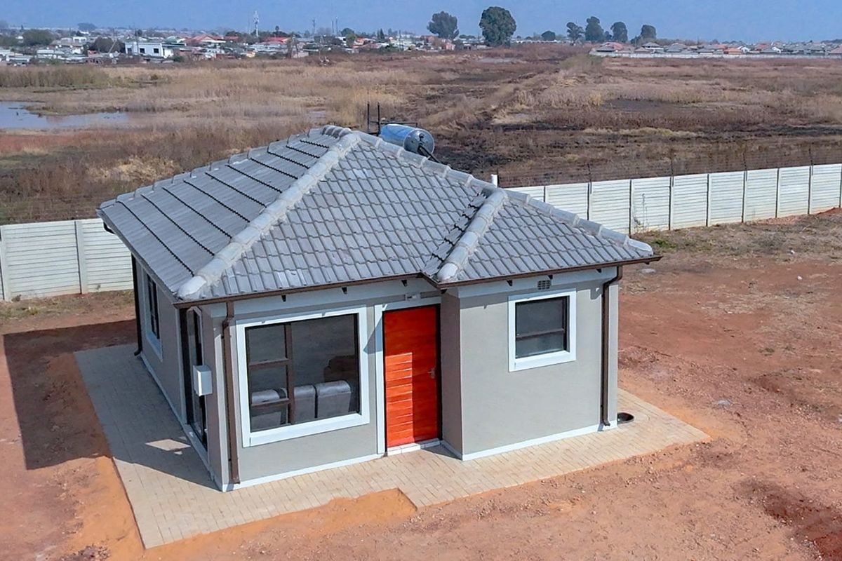 Aerial view of a modern detached house featuring a tiled roof, solar geyser, and paved perimeter, set within a fenced residential plot.