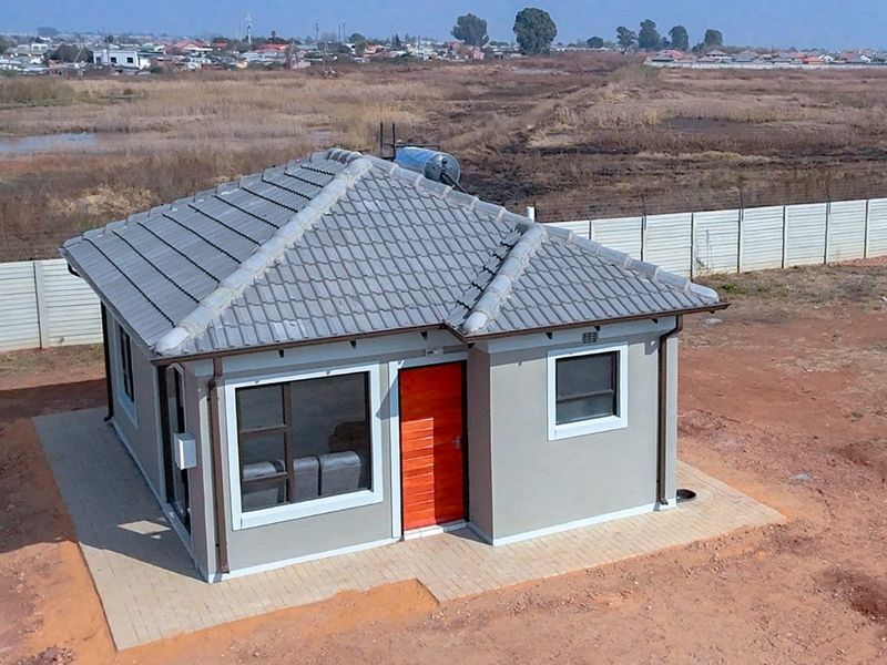 Aerial view of a modern detached house featuring a tiled roof, solar geyser, and paved perimeter, set within a fenced residential plot.