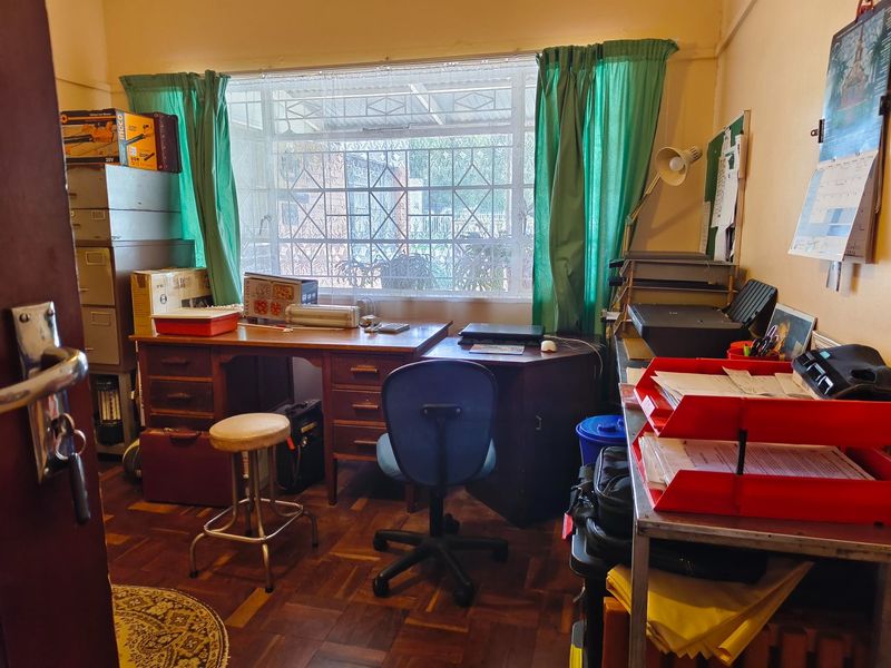 A functional home office space featuring classic parquet flooring and a large window fitted with security burglar bars.