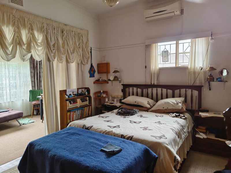 A bedroom featuring a split-system air conditioner, security bars on the window, and a classic picture rail, with an adjoining sunroom area.
