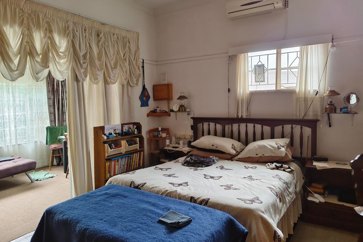 A bedroom featuring a split-system air conditioner, security bars on the window, and a classic picture rail, with an adjoining sunroom area.