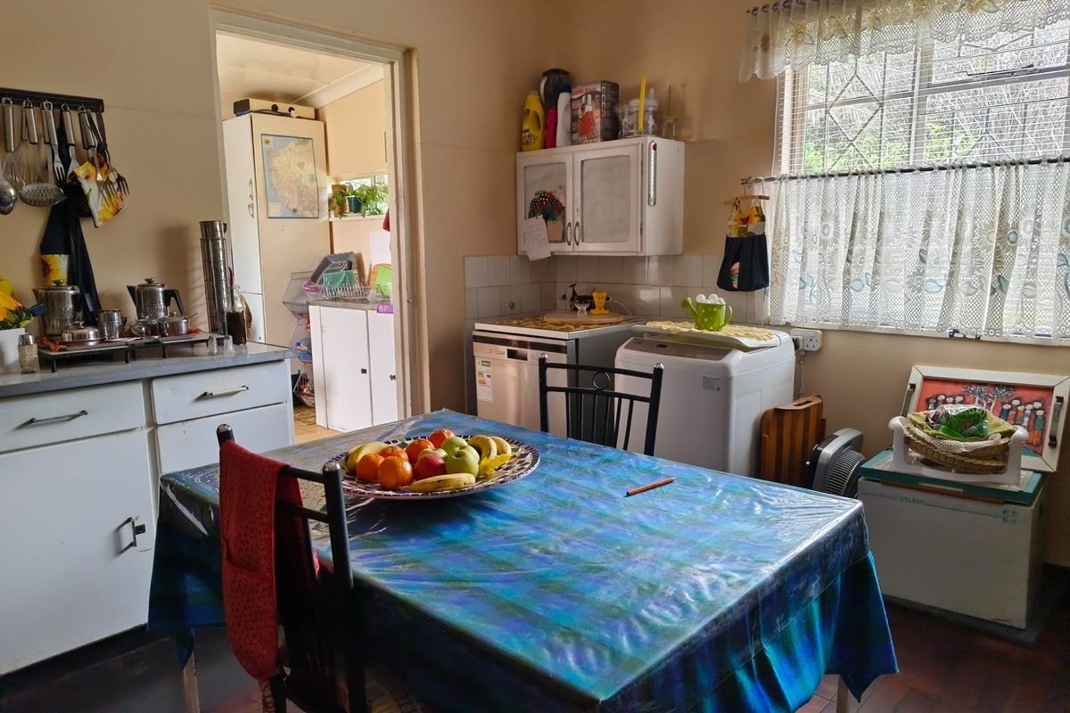 A functional kitchen featuring built-in cabinetry, tiled splashbacks, and parquet flooring, with an adjacent utility area visible through the doorway.