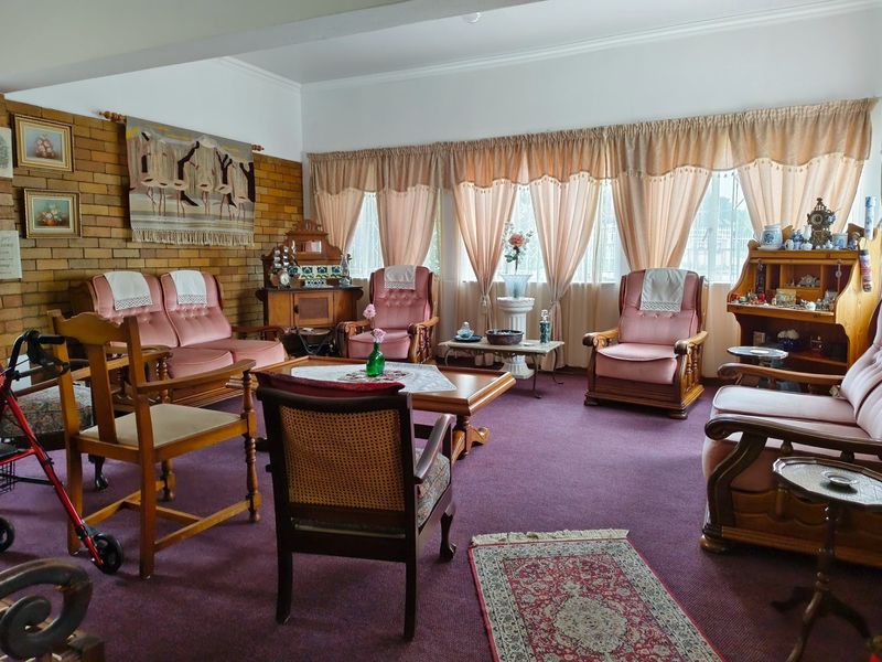 Spacious living room featuring an exposed brick accent wall and large windows, offering a traditional layout with carpeted flooring.