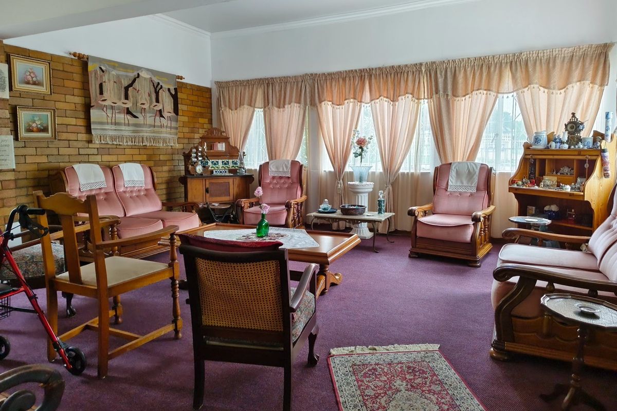 Spacious living room featuring an exposed brick accent wall and large windows, offering a traditional layout with carpeted flooring.