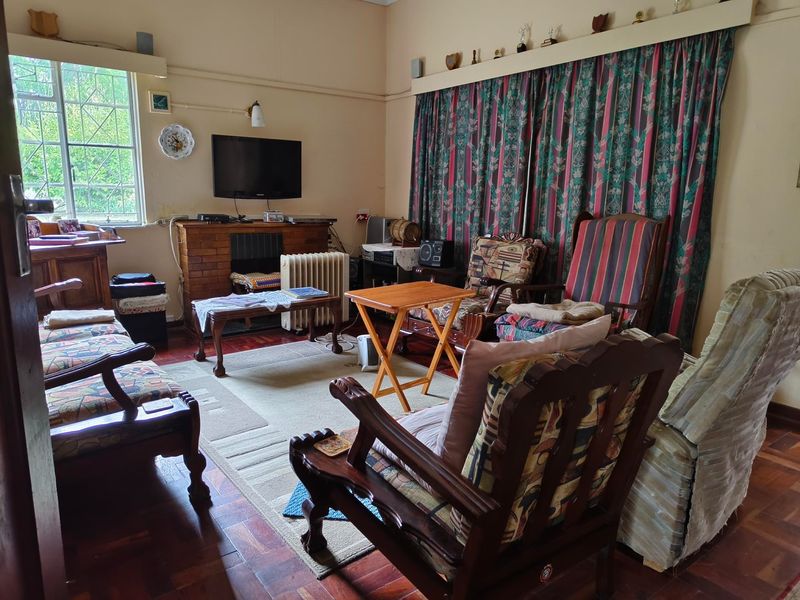 A traditional living room featuring parquet flooring, a brick fireplace, and a large window, offering a dated but functional space with potential for modernization.