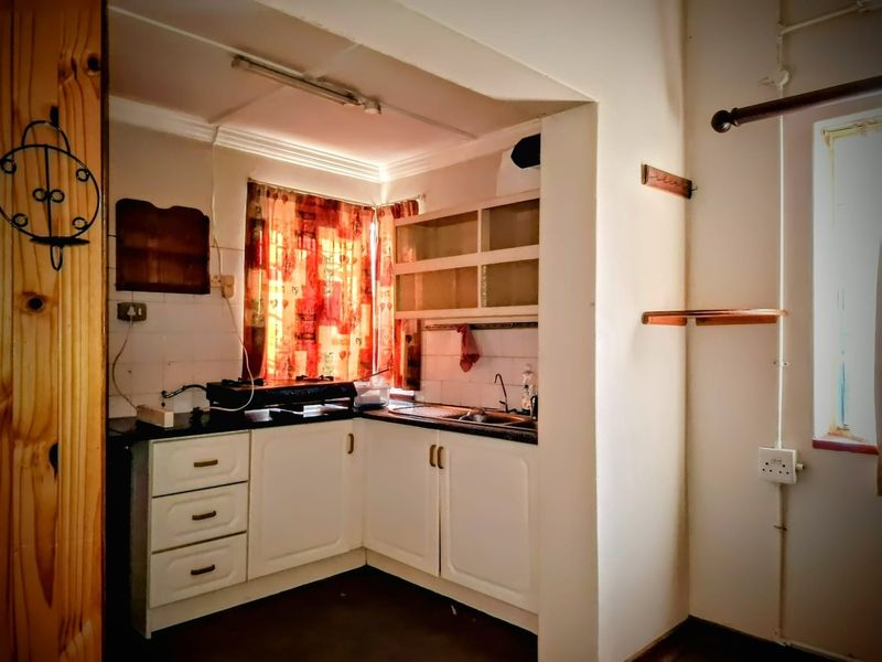 A compact kitchen featuring white built-in cabinetry, a stainless steel sink, and tiled backsplash, offering a functional layout in need of cosmetic updates.