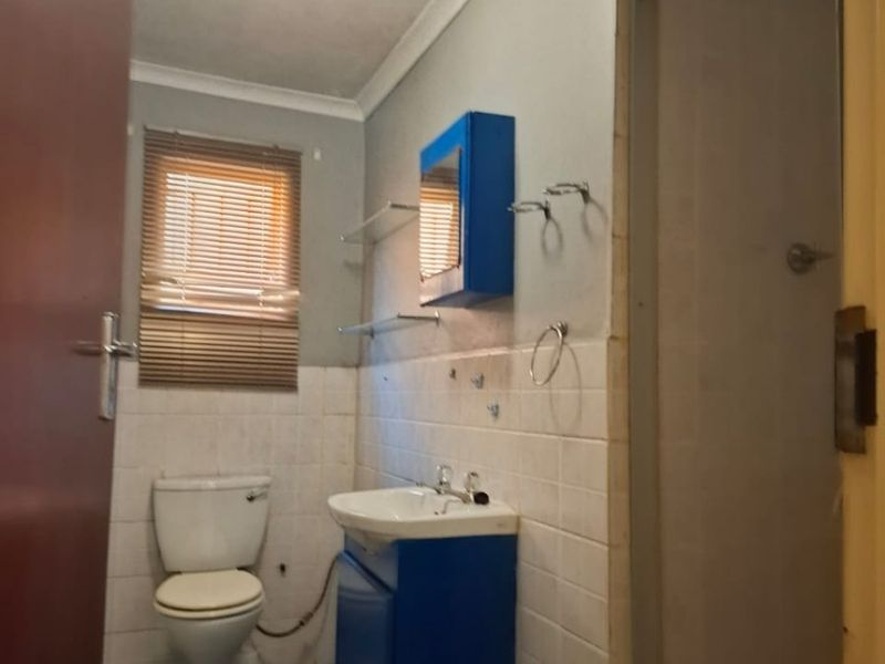 A functional bathroom featuring a shower enclosure, vanity basin, and toilet with tiled finishes, offering potential for modernization and cosmetic updates.