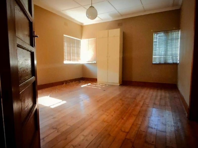 An empty bedroom featuring original timber flooring, a built-in wardrobe, and natural light through venetian blinds.