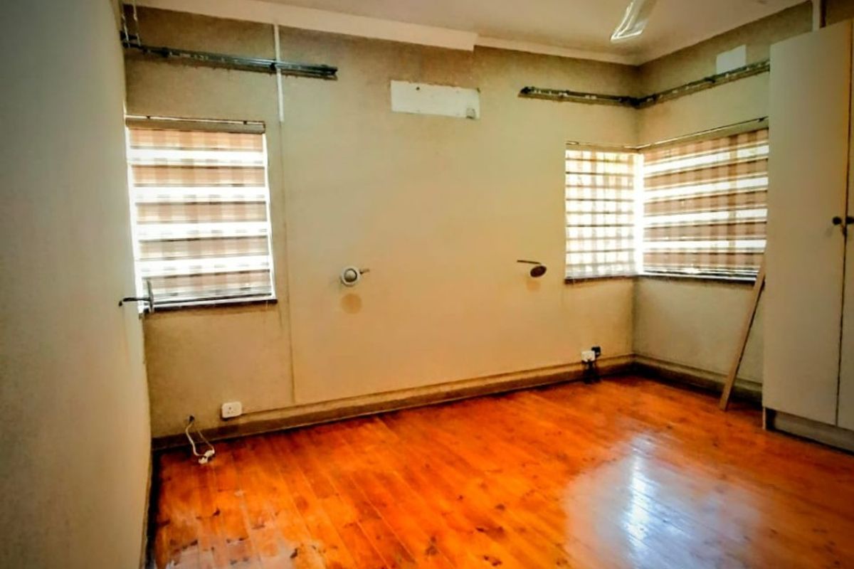 An empty bedroom featuring polished timber flooring, a ceiling fan, and built-in wardrobe, currently requiring cosmetic wall repairs and finishing.