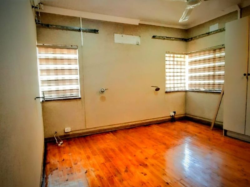 An empty bedroom featuring polished timber flooring, a ceiling fan, and built-in wardrobe, currently requiring cosmetic wall repairs and finishing.