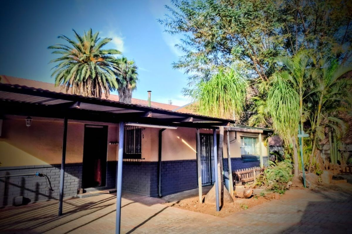Rear exterior view of the house featuring a covered patio area, paved ground, and established garden surroundings.