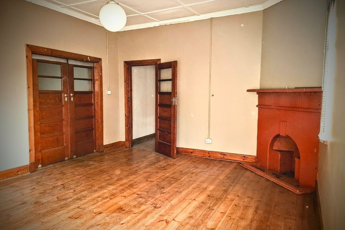 An empty living room featuring original hardwood flooring, a traditional fireplace, and classic timber door frames, offering a blank canvas for renovation.