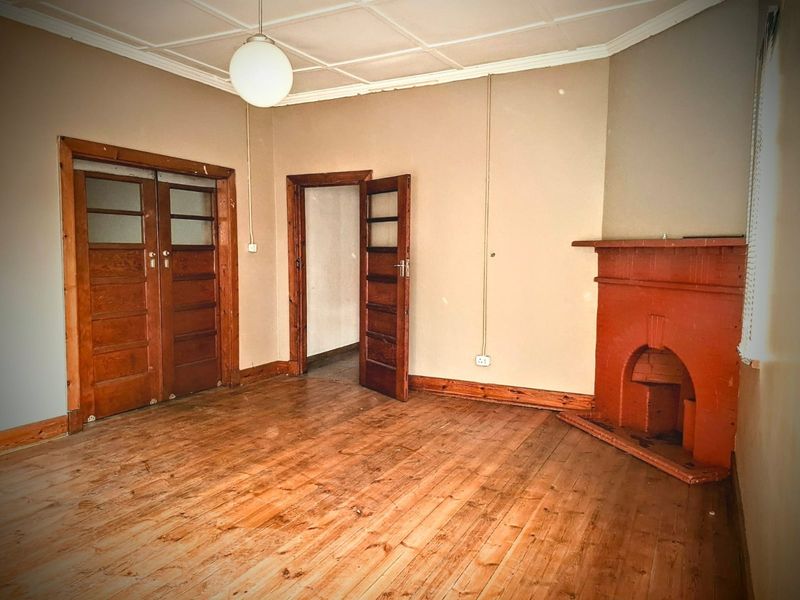 An empty living room featuring original hardwood flooring, a traditional fireplace, and classic timber door frames, offering a blank canvas for renovation.