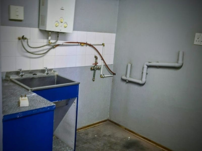 A functional laundry area featuring a stainless steel sink, gas geyser, and exposed plumbing connections, ready for modernization.