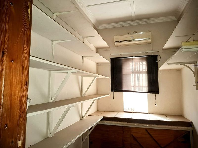 A functional scullery or pantry area featuring extensive wall-mounted shelving, a tiled countertop, and a wall-mounted air conditioning unit.