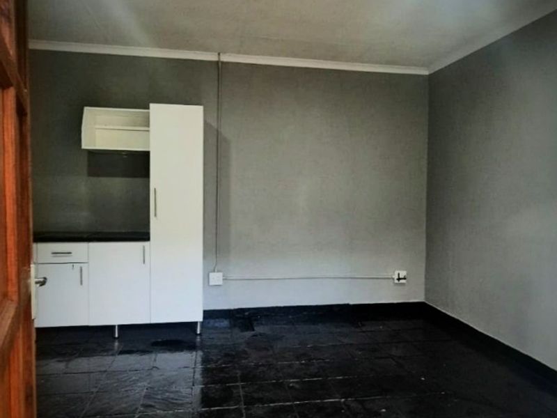 A compact, empty kitchen area featuring basic built-in cabinetry, dark tiled flooring, and exposed surface wiring.