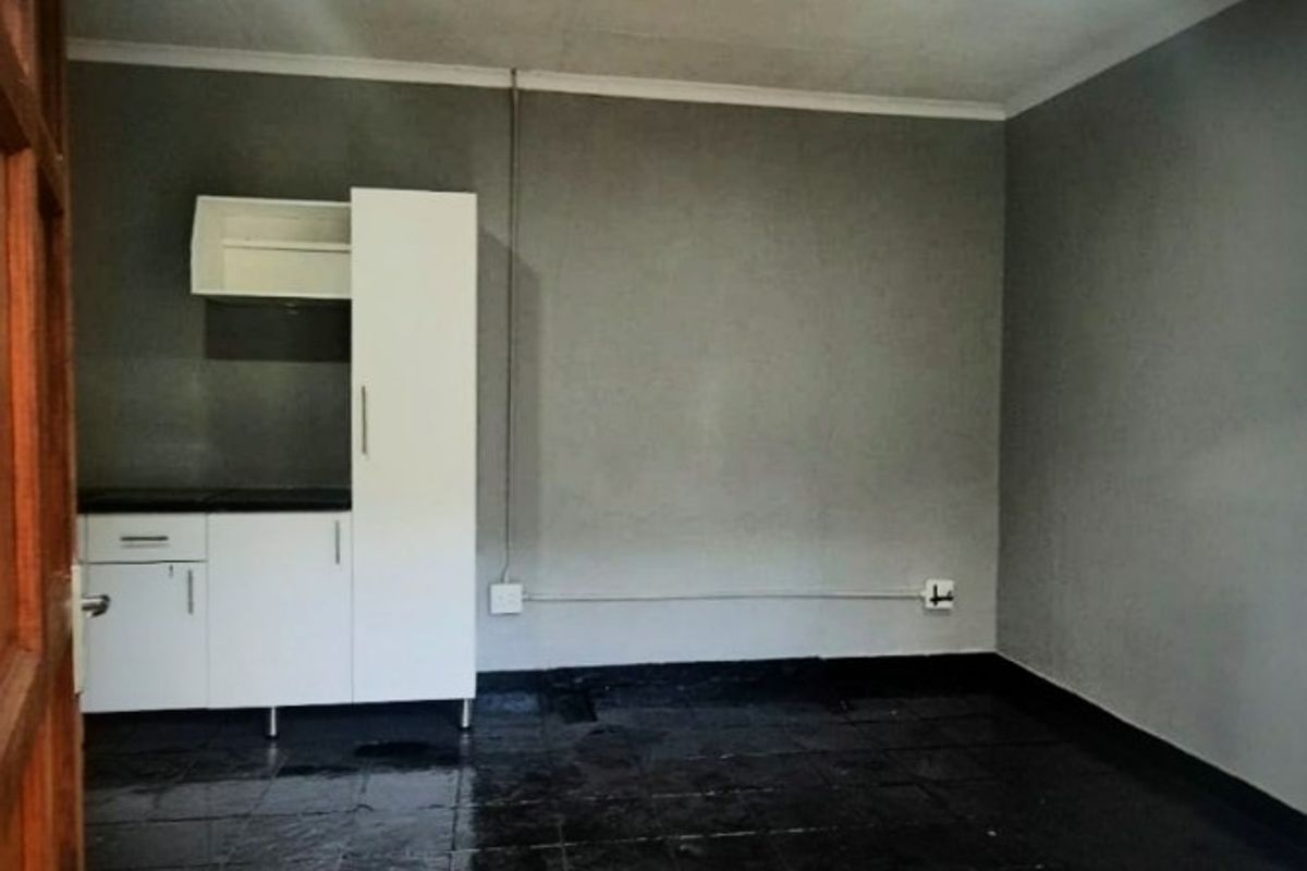 A compact, empty kitchen area featuring basic built-in cabinetry, dark tiled flooring, and exposed surface wiring.