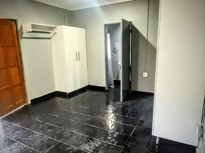 An empty bedroom featuring dark tiled flooring, built-in cupboards, and direct access to an en-suite bathroom.
