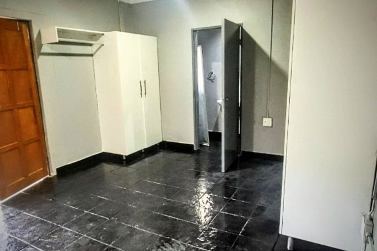 An empty bedroom featuring dark tiled flooring, built-in cupboards, and direct access to an en-suite bathroom.