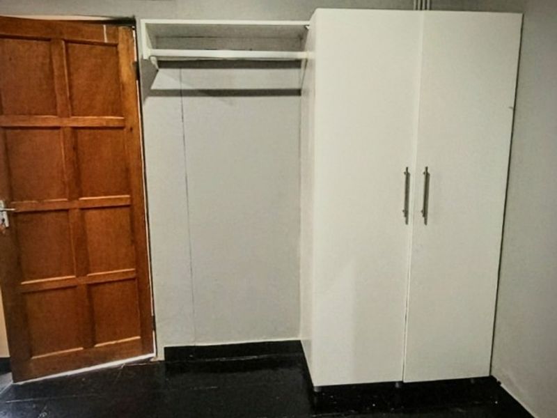 A simple bedroom featuring dark tiled flooring, a timber door, and a built-in wardrobe with an integrated hanging rail.