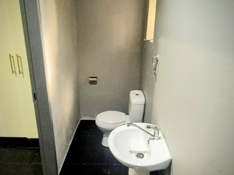 A compact guest bathroom featuring a pedestal basin and toilet with dark tiled flooring and neutral wall finishes.