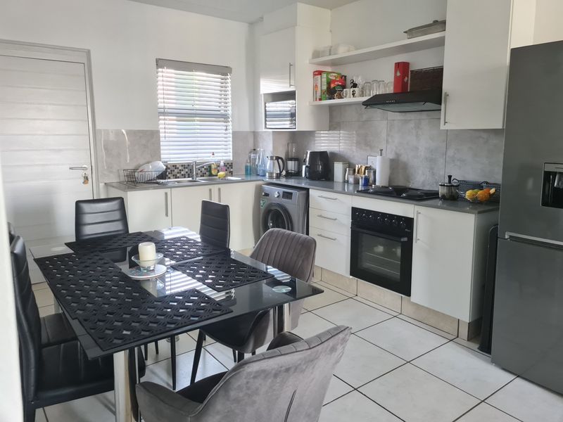 Open-plan kitchen and dining area featuring modern white cabinetry, tiled flooring, built-in oven, hob, extractor fan, and a functional laundry connection.