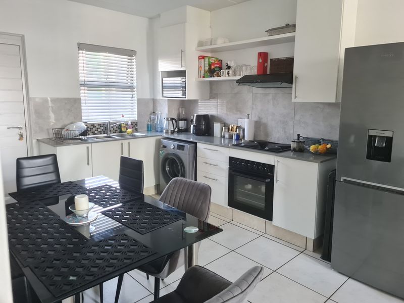 Open-plan kitchen featuring white cabinetry, tiled splashbacks, integrated oven and hob, and tiled flooring, seamlessly connected to the dining area.