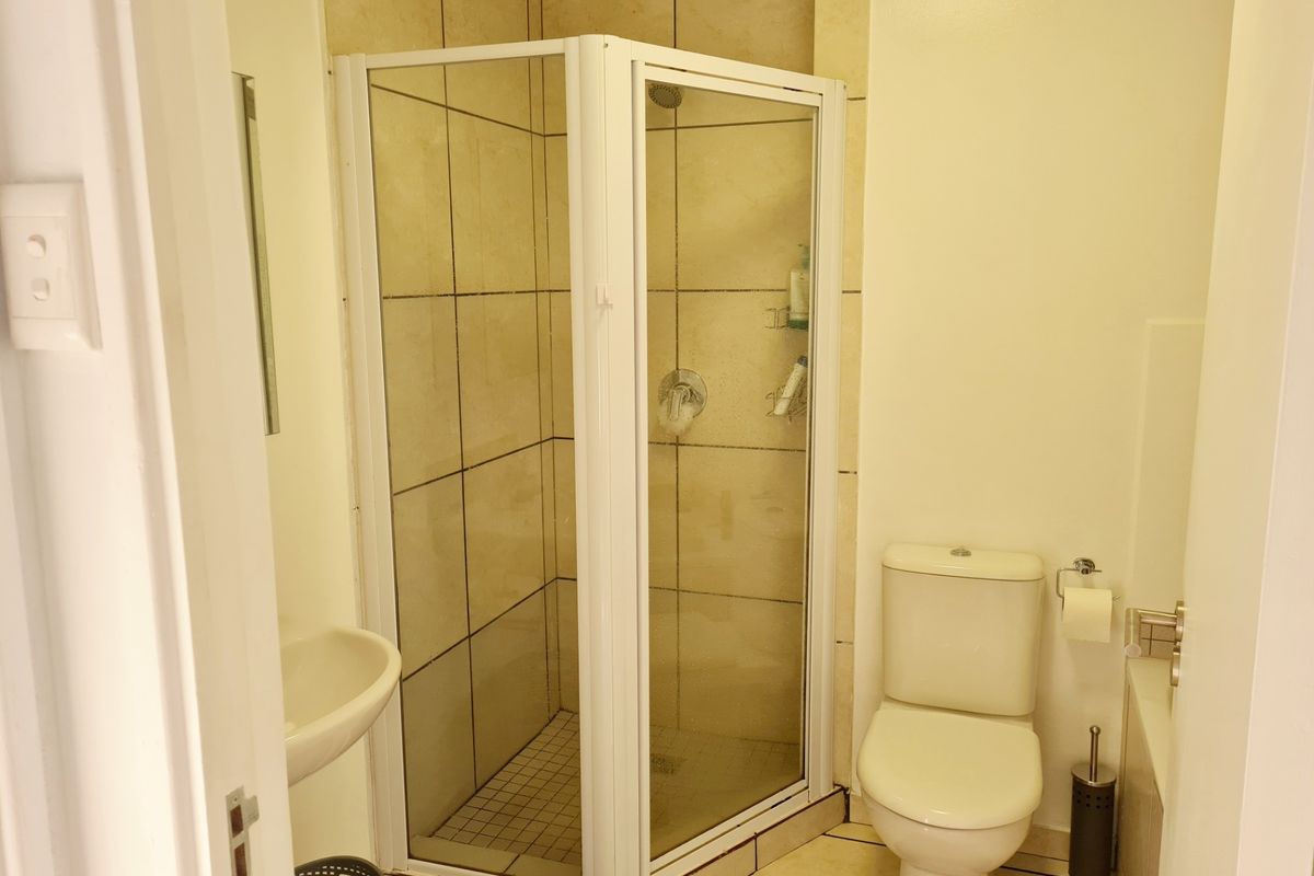 A functional bathroom featuring a corner shower enclosure, a standard toilet, and a wall-mounted basin with neutral wall and floor tiling.