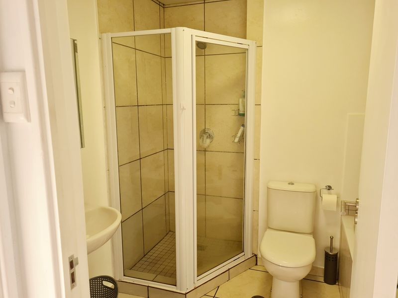A functional bathroom featuring a corner shower enclosure, a standard toilet, and a wall-mounted basin with neutral wall and floor tiling.