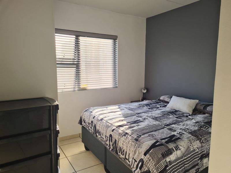 A well-lit bedroom featuring neutral walls, a dark grey accent wall, tiled flooring, and fitted venetian blinds.