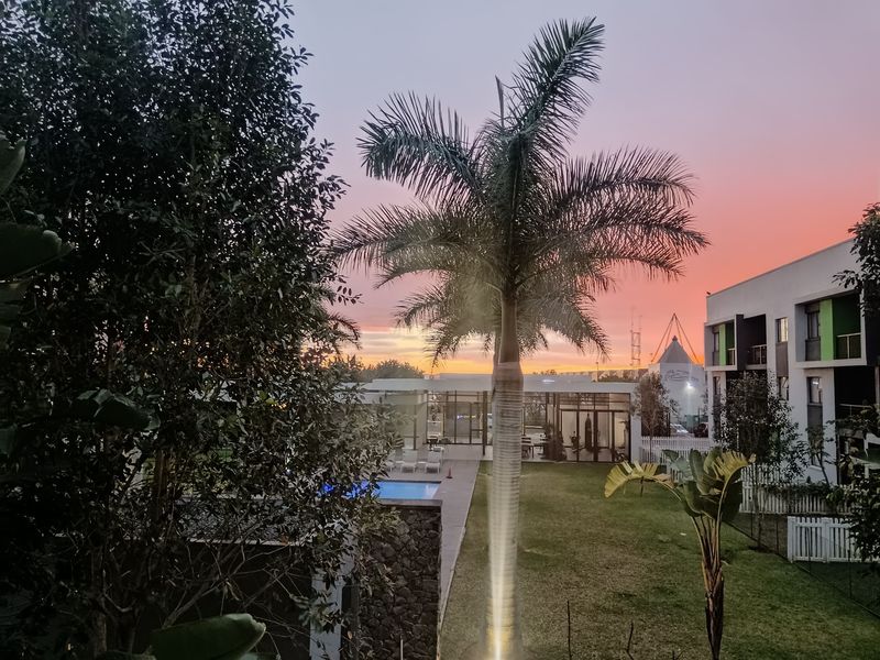 A scenic sunset view overlooking a communal garden, swimming pool area, and modern apartment complex architecture.