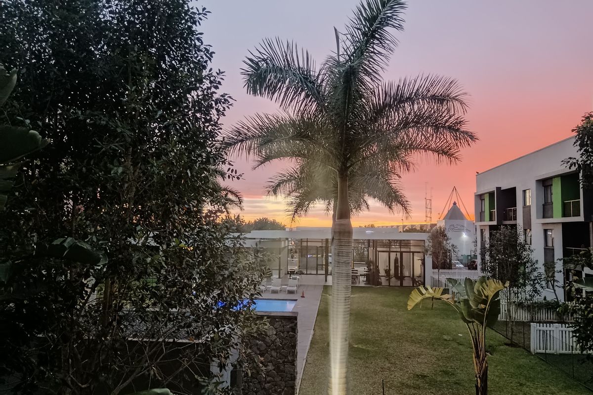 A scenic sunset view overlooking a communal garden, swimming pool area, and modern apartment complex architecture.