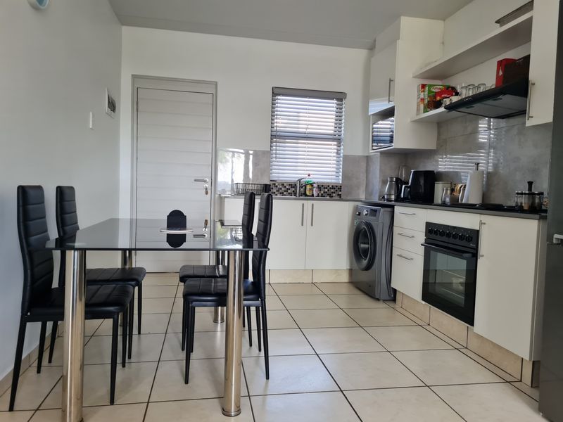 Open-plan kitchen and dining area featuring modern white cabinetry, integrated oven, extractor fan, and tiled flooring with a functional layout.