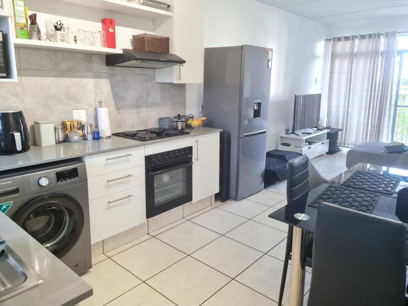 An open-plan kitchen and living area featuring modern cabinetry, stone countertops, a gas hob, and tiled flooring, leading to a balcony.