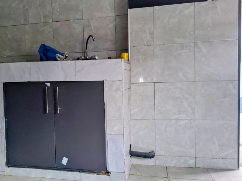 A basic kitchen area featuring tiled surfaces, built-in cabinetry, and a sink, currently in need of cosmetic updates and finishing touches.