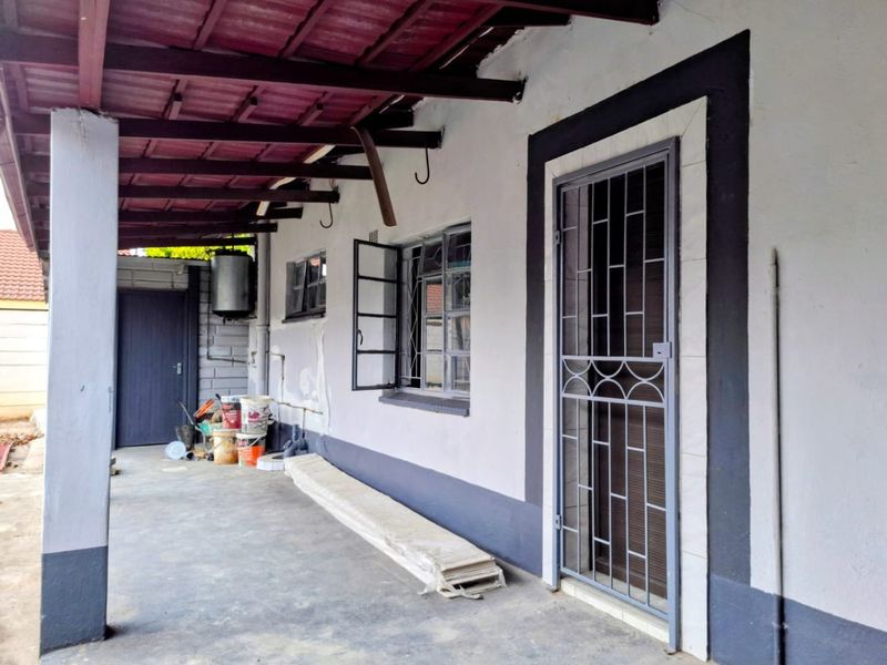 A covered outdoor patio area featuring concrete flooring, security gate access, and exposed roof rafters, requiring some maintenance and cosmetic updates.