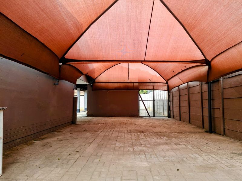 A covered outdoor parking area featuring paved flooring, a shade cloth canopy, and secure metal gate access.