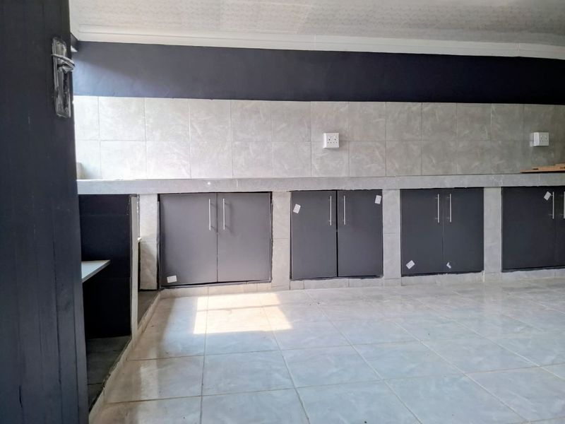 An empty kitchen area featuring built-in concrete-style cabinetry, tiled backsplash, and tiled flooring, awaiting final finishes and appliance installation.