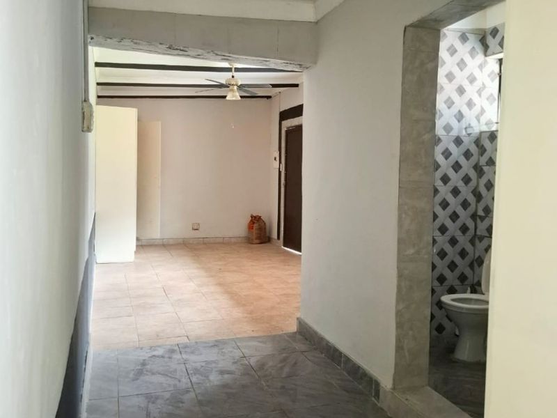 A vacant hallway area featuring tiled flooring and a ceiling fan, with an adjacent bathroom visible through an open doorway.
