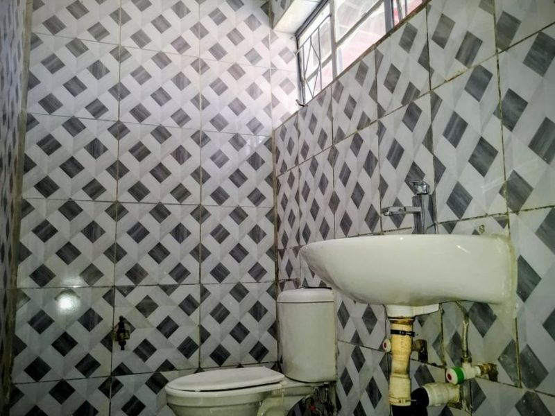 A compact bathroom featuring a wall-mounted basin and toilet with full-height patterned wall tiling and a top-hung window with security bars.