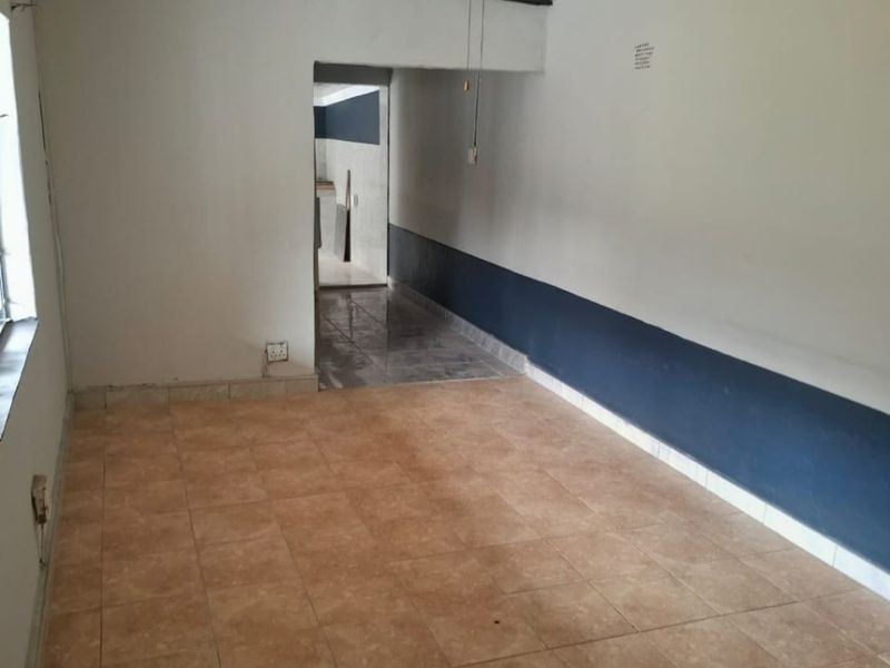 An empty living room featuring tiled flooring, a ceiling fan, and two-tone wall paint, leading into an adjacent tiled area.