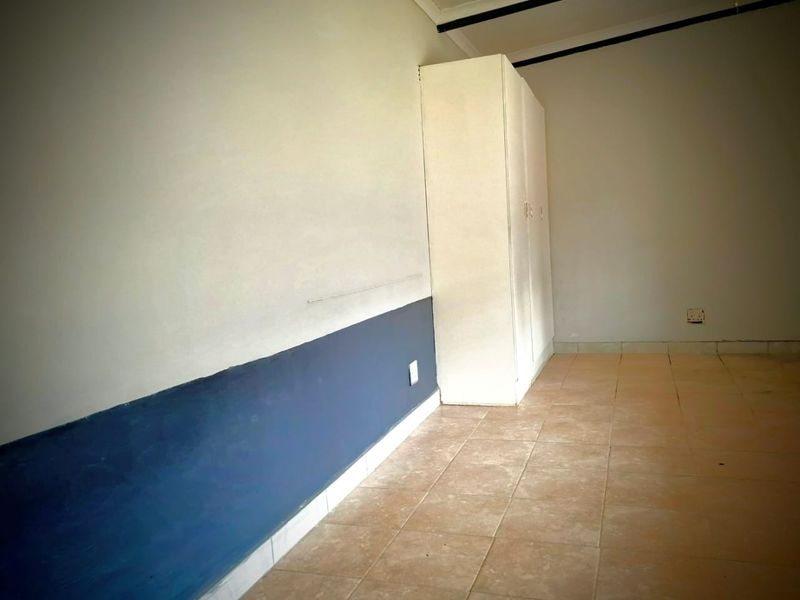 An empty bedroom featuring tiled flooring and a built-in wardrobe, requiring cosmetic updates to the wall finishes.