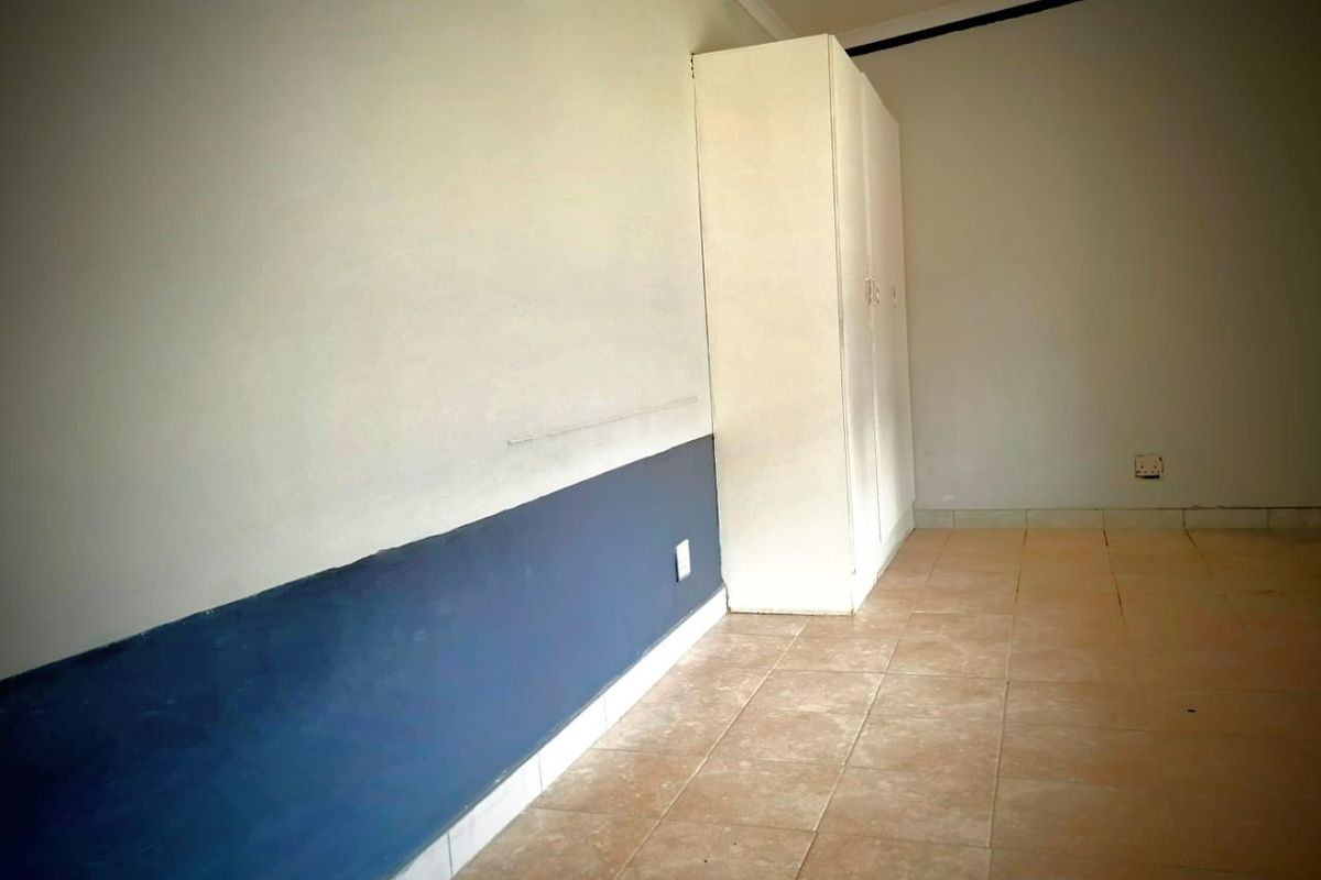An empty bedroom featuring tiled flooring and a built-in wardrobe, requiring cosmetic updates to the wall finishes.