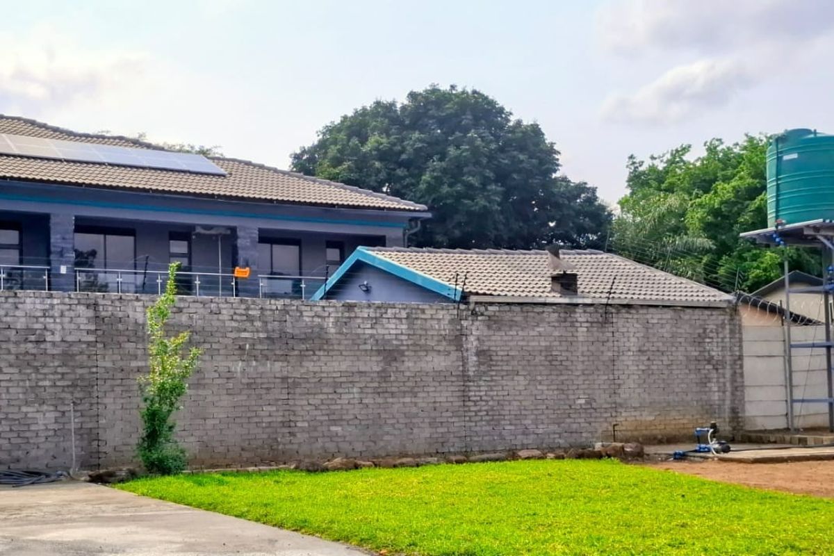 Rear view of the property featuring a large brick boundary wall, solar panels on the roof, and an elevated water storage tank.