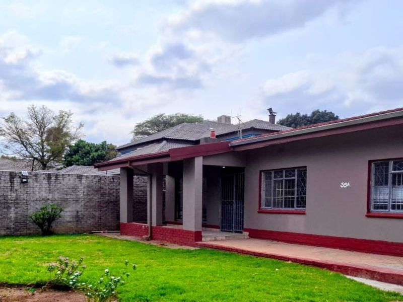 Rear view of the house featuring a covered patio, lawn area, and brick boundary wall with security bars on the windows.